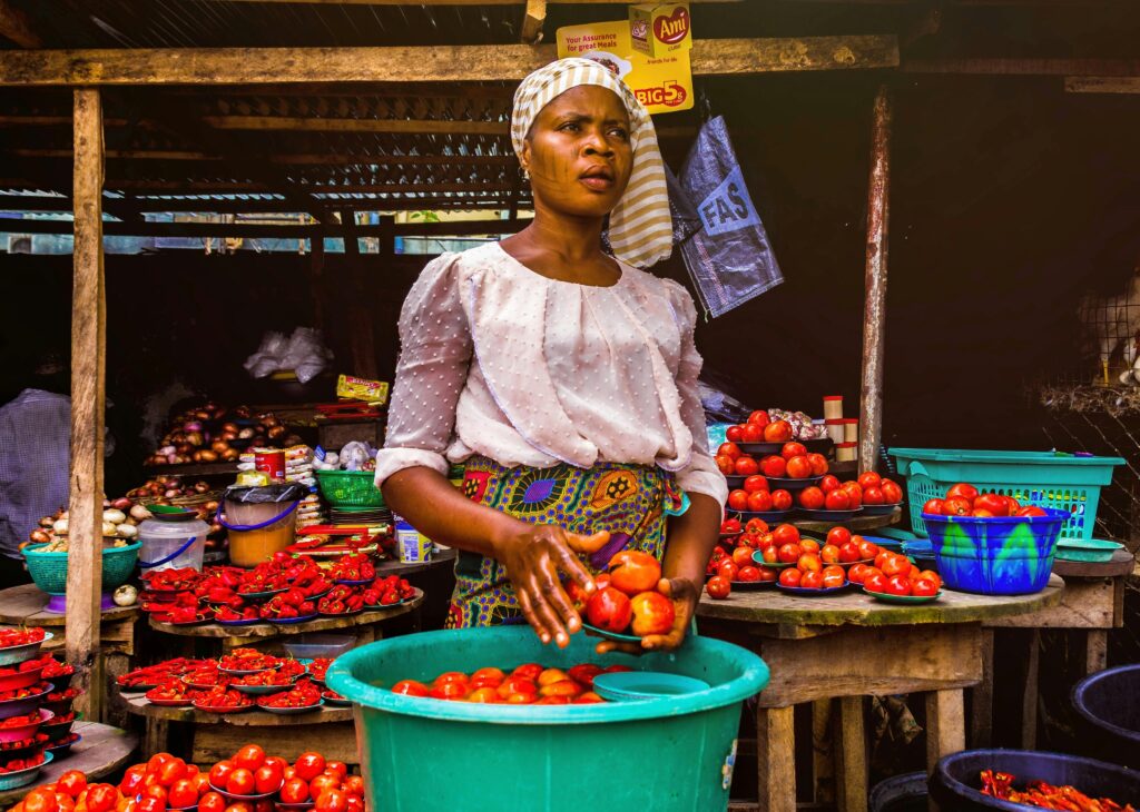 pexels-photo-3213283-3213283 Woman selling fresh tomatoes at an outdoor market stall, showcasing vibrant produce.